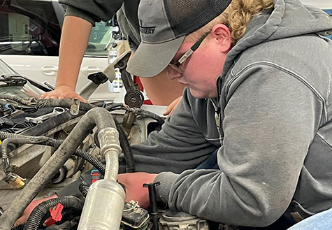Student working under the hood on a car engine